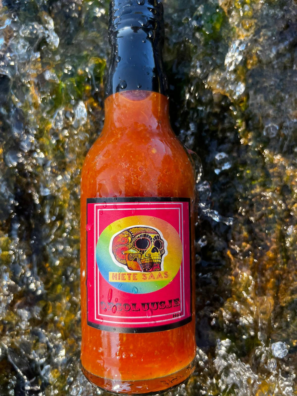 Bouteille de sauce piquante Opsoluusje avec étiquette colorée sur un fond naturel.